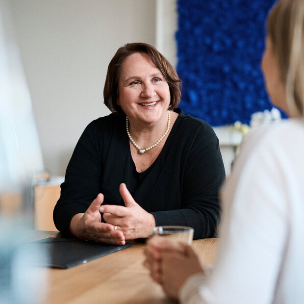 Ministerin Theresa Schopper im Gespräch mit einer Frau, die man von hinten sieht. Schopper redet deutlich mit den Händen.